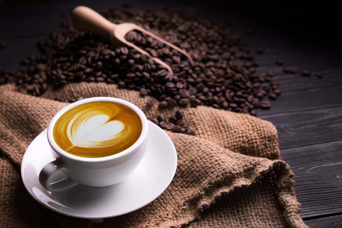 a cup of coffee with an artistic design next to a pile of coffee beans