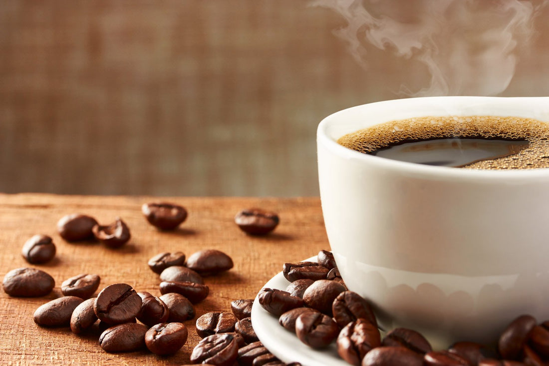 a cup of black coffee next to some spilled coffee beans